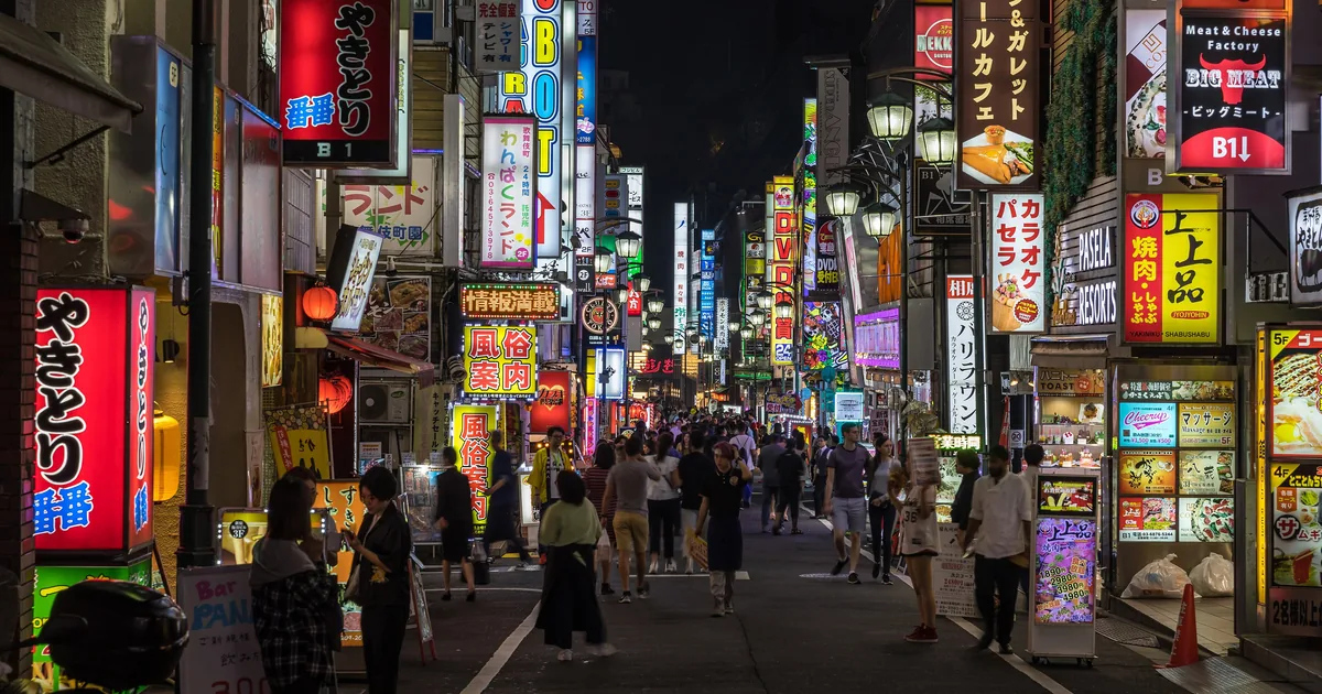 Calle de Kabukichō, en Tokio, con las fachadas cubiertas de rótulos luminosos y gente caminando por el centro de la calzada.