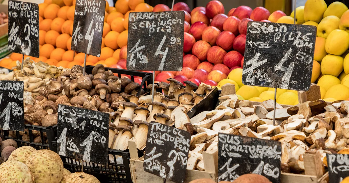 Puesto del Naschmarkt de Viena con setas, fruta y verdura, y los precios escritos a mano en pizarras.