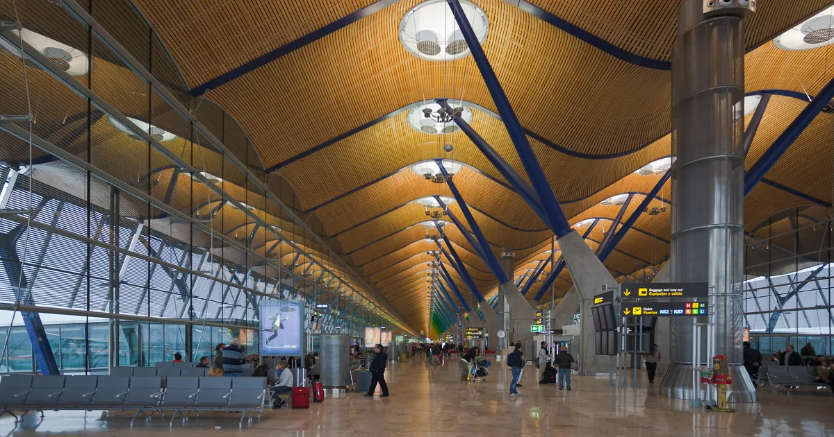 Vestíbulo de la Terminal 4 de Madrid-Barajas, con su cubierta ondulada de bambú y viajeros cruzando con equipaje.
